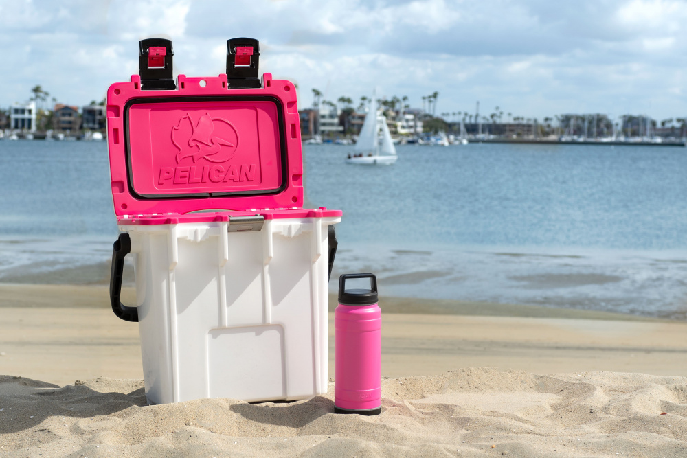 White cooler with pink interior on a beach with a matching pink tumbler.